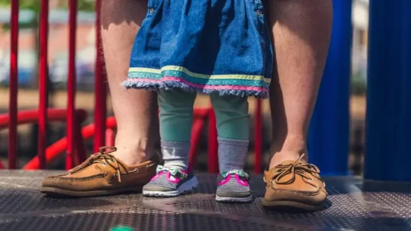 la foto mostra le gambe di una bambina in piedi fra le gambe del papà per rappresentare l'assistente all'infanzia