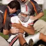 un giocatore di football americano seduto sul campi mentre il personale medico interviene