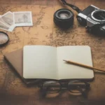 una scrivania con una mappa, un diario, una macchina fotografica e altri accessori per un viaggio, l'immagine rappresenta il corso di scienze del turismo
