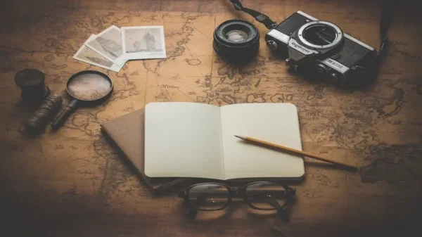 una scrivania con una mappa, un diario, una macchina fotografica e altri accessori per un viaggio, l'immagine rappresenta il corso di scienze del turismo