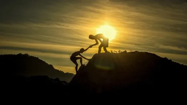 una persona aiuta un compagno a scalare una cima, l'immagine rappresenta il corso di travel coach e consulente di viaggio