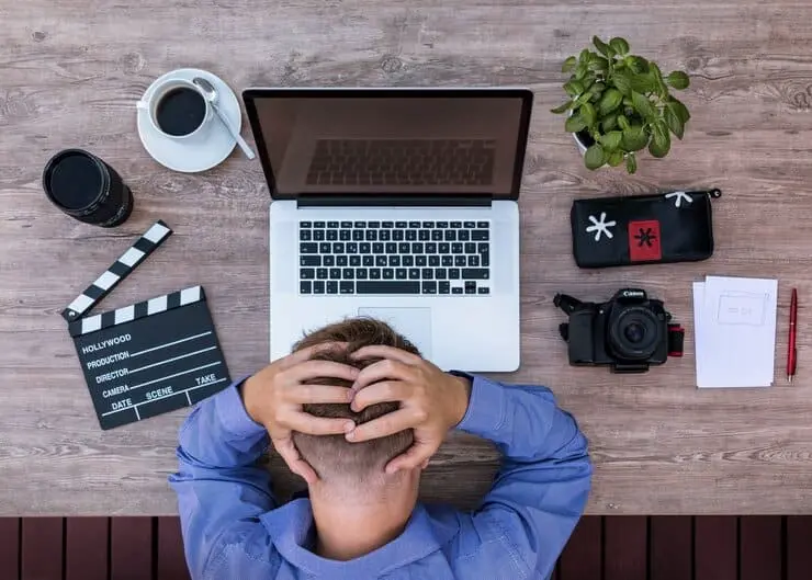 un uomo difronte a un computer su una scrivania sta col capo chinato con le mani tra i capelli