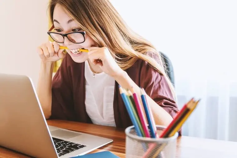 una ragazza ad una scrivania che osserva un computer mentre morde una matita